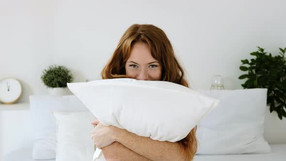 portrait woman sits relaxed on bed and playfully  hugs  comfortable pillow