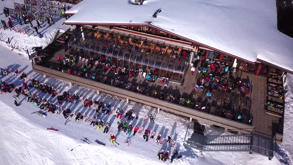 Aerial drone video of crowded ski restaurant with terrace full of people. Apres ski bar surrounded b alt