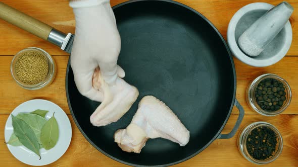 The cook puts the chicken wings in the pan. Chicken wings in a cast iron skillet ready to marinate