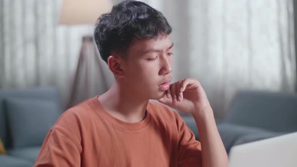 Close Up Of Asian Boy Footwear Designer Thinking While Working On A Laptop At Home alt