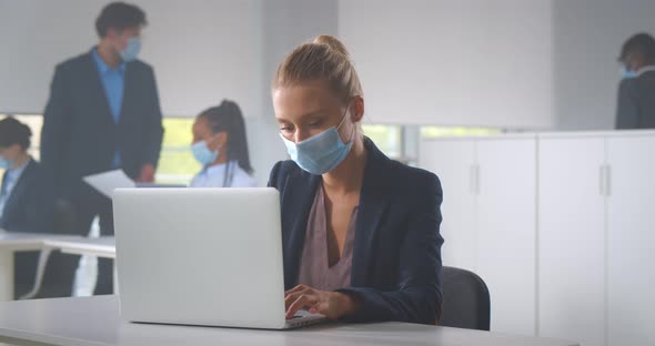 Businesswoman Sitting in Office in Front of Computer Wearing Face Mask alt