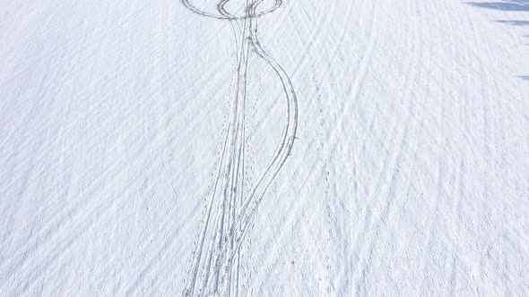 Flying over tire trails and foot steps in snow 4K drone video alt