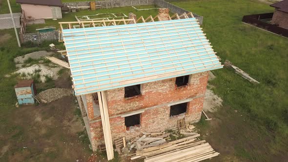 Aerial view of a brick house with wooden roof frame under construction. alt
