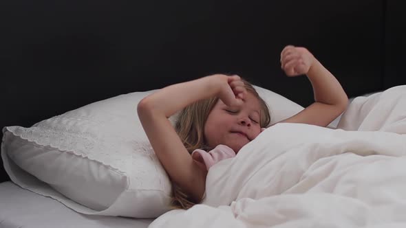 Happy Girl Child Waking Up Stretching Arms on the Bed in the Morning