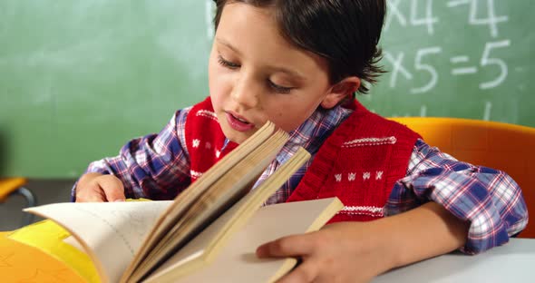 Schoolboy reading book in classroom at school alt