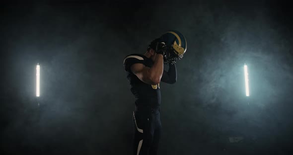 American Football Sportsman Player Putting on and Tightening His Football Helmet on Black Background alt