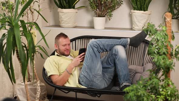 Man Chatting Using Smartphone Lying on Sofa at Home Types Message with Happy Smile