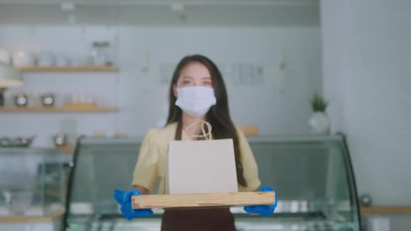Attractive asian female cafe worker wears face mask and gloves giving takeaway food bag