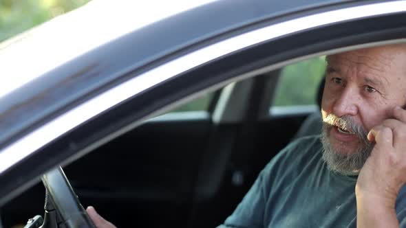 Old man is talking on the phone in his car. alt