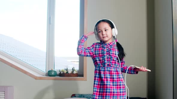 Cheerful Asian Girl in Headphones Dancing on Bed