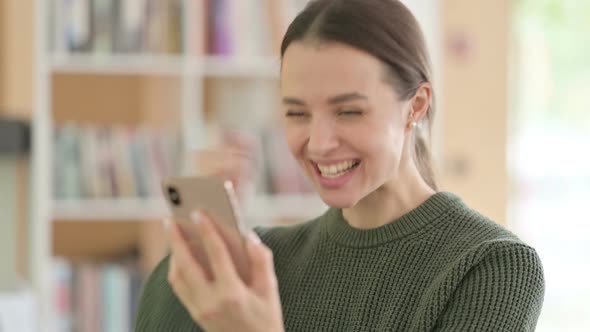 Young Woman Celebrating Online Success on Smartphone alt