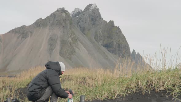 Man Preparing Drink In Wilderness Around Vestrahorn Mountain alt