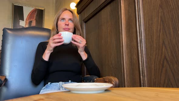 Woman Picks Up A Cup Of Coffee From The Table And Takes A Sip
