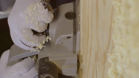 Vertical Shot Closeup Hands of Carpenter Using Electric Planer with Wooden Blank in Workshop