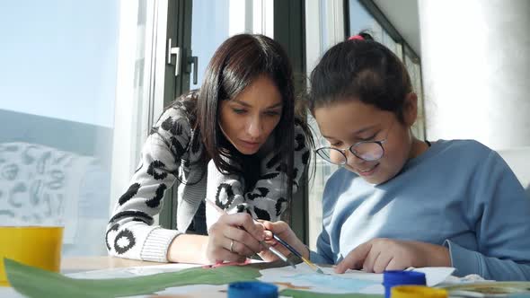 A Young Mother and Daughter Paint a Picture with Paint on Paper Near the Panoramic Window
