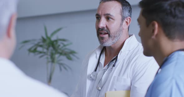 Senior caucasian male doctor discussing with diverse colleagues at a hospital staff meeting alt