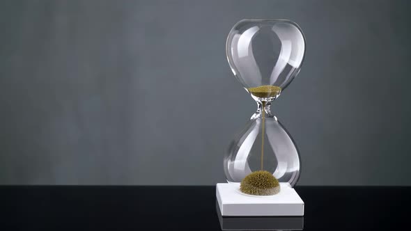 An Hourglass Made of Yellow Metal Shavings Passes Through a Funnel Symbolizing the Concept of Time alt