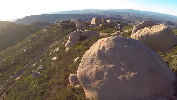 Aerial shot of young man mountain biker resting with his bike on a boulder. alt