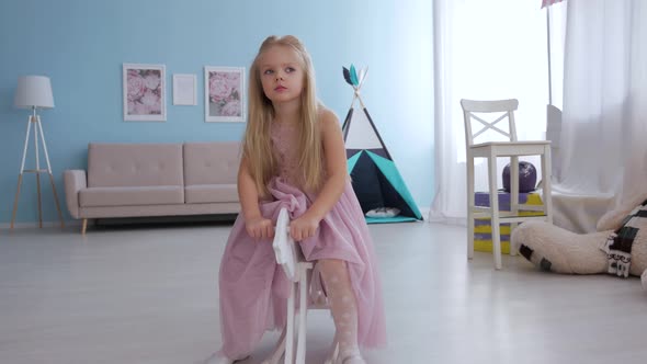 Pretty little girl in purple dress with long blond hair rides toy horse in room