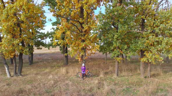 Aerial Drone View of Woman Riding Bicycle on Countryside Road with Blue Sky Background alt