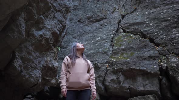 Brunette Woman in Hoodie Looks Up in a Rocky Gorge alt