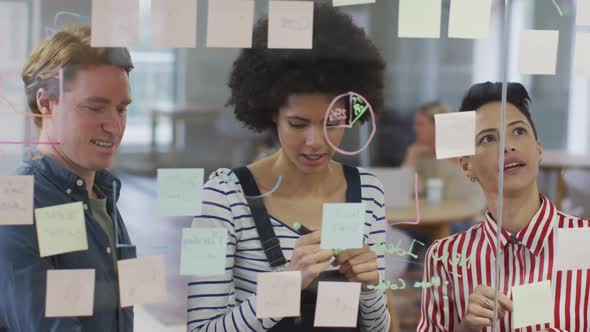 Diverse male and female business colleagues discussing by glass wall with memo notes alt