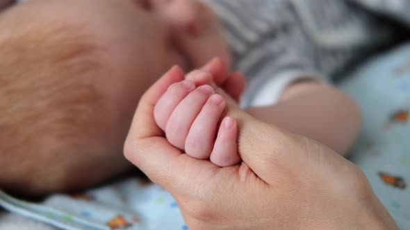 Cute sleeping newborn baby holds mother finger