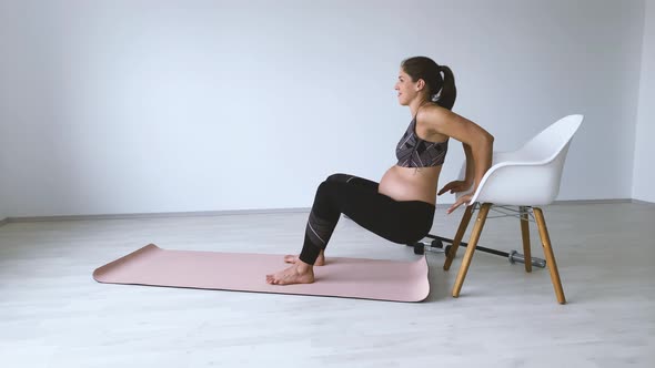 Slow motion shot of pregnant woman during exercise on mat and chair