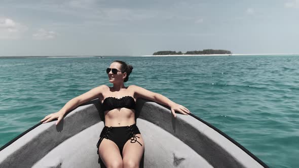 Young Woman in a Bikini and Sunglasses Lies on the Bow of Boat Floating By Ocean alt
