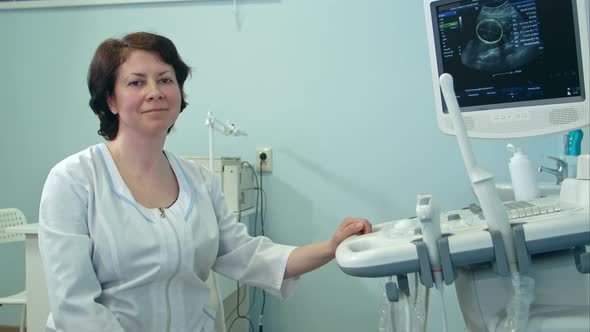 Smiling Female Doctor Sitting Next To Ultrasound Diagnostic Device alt