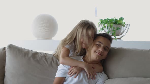 Sister and Brother Sitting on the Sofa with Pillows in the Cozy Room and Hugging