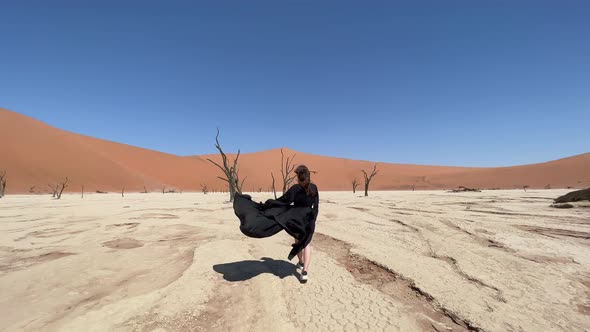 A Young Woman in a Long Black Dress Walks Through the Desert