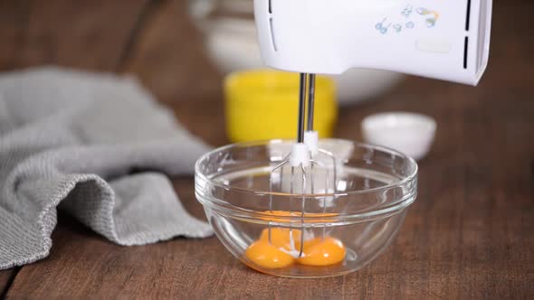 Closeup of the Process of Beating Egg Yolks with Sugar with Electric Mixer in a Glass Bowl