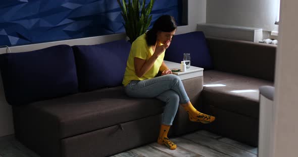 Woman sitting on sofa cough and drink water in the living room near cat alt