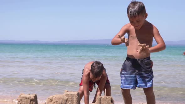 Two caucasian boys at beach of Stoupa, Peloponnese, Greece, one is building a sand castle and the ot alt