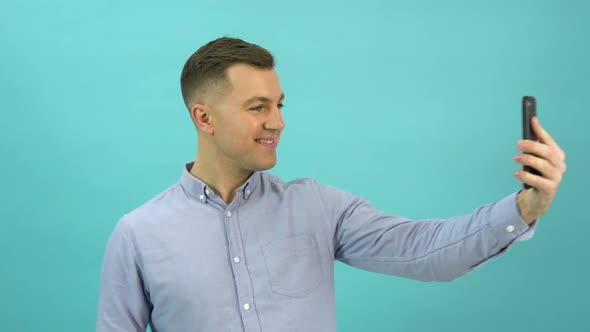 Caucasian Middleaged Man in a Blue Shirt is Video Calling on His Smartphone and Expressing Joy alt