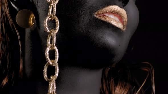 Closeup of a Woman with Black and Gold Paint and a Gold Chain Posing in Studio alt