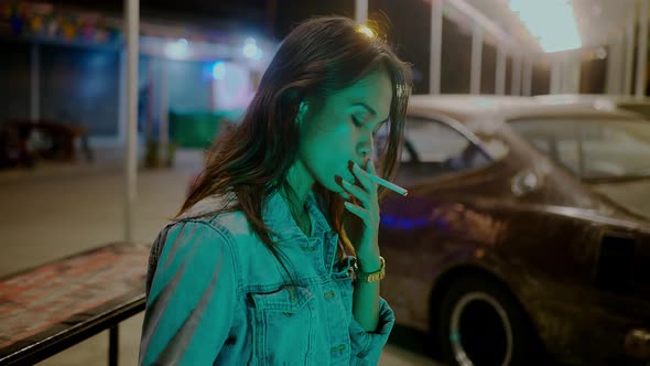 A Girl Smokes in Front of a Rusty Classic Car While Typing a Message Late at Night alt