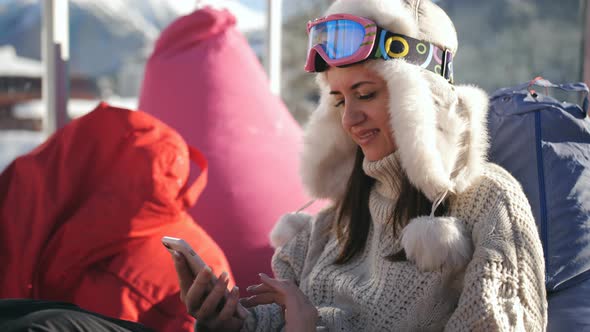 A Girl Uses a Smart Phone Sitting in a Cafe at a Ski Resort