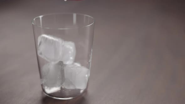 Slow Motion Man Add Ice Cubes Into Tumbler Glass on Walnut Table with Copy Space