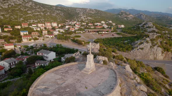 Drone Overflight of a Cross with Jesus on Top of a Mountain Hill with a View of the Sea at Sunset