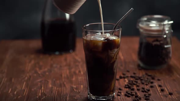 Slow Motion of Cream Being Poured Into a Tall Glass of Cold Brew Iced Coffee on Brown Wood Table