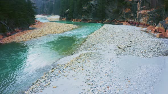 Bhagirathi river flowing mid of rocks surrounded by sand, small pebbles and pine trees in Harshil