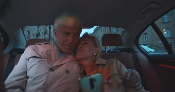 Senior Couple Sitting on Backseat in Car and Using Smartphone alt