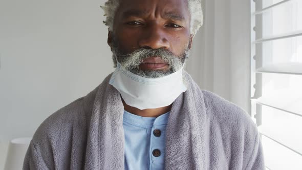 Senior man with face mask on his chin at home alt