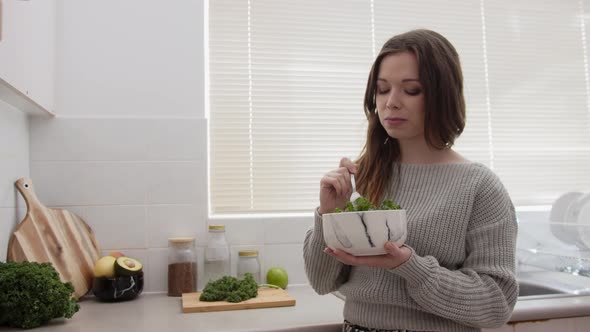 Girl eating salad and enjoying the food in the bright kitchen. Vegetarian, healthy and raw food