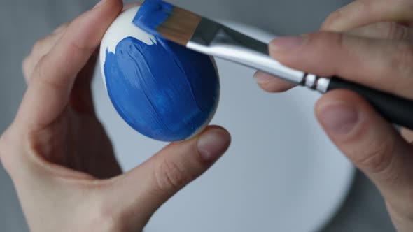 Close-up. Female hands paint Easter egg in a modern minimalist style with colorful paint.