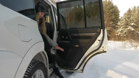 Young Woman Sitting in Car Cleaning Snow From Legs After Winter Walk in Park alt