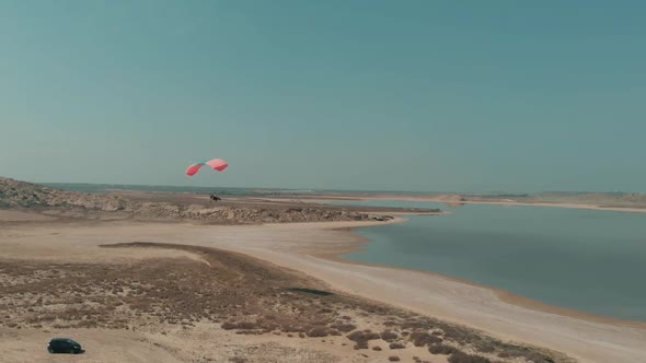 Aerial View Of Motorised Paraglider Flying Over Arid Coastline Next To Salt Lake. Follow Shot alt