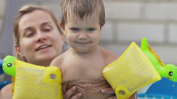 Mom Plays with a Naked Baby in Oversleeves in the Pool Against the Background of a Summer Sunset alt